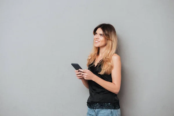 Young woman holding mobile phone and looking up at copyspace — Zdjęcie stockowe