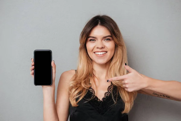 Mulher bonita de sorriso que aponta o dedo no telefone móvel da tela em branco — Fotografia de Stock