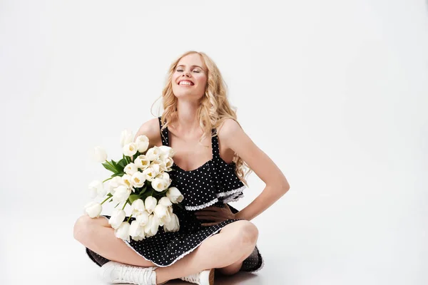 Lachende blonde vrouw zittend op de vloer met boeket bloemen — Stockfoto