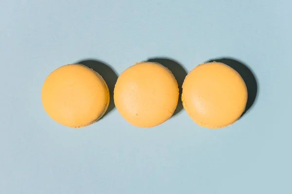 Tres macarrones amarillos dulces sobre fondo de mesa azul . — Foto de Stock