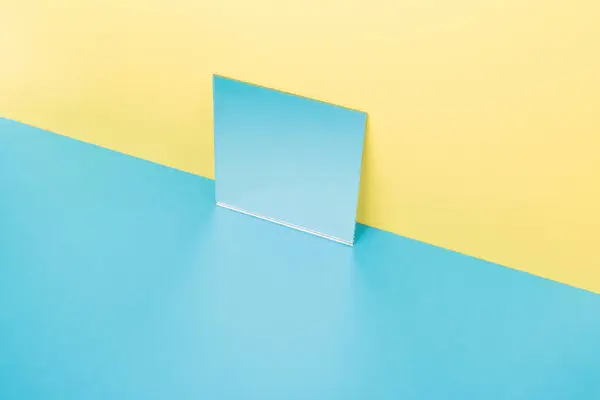 Mirror on blue table isolated over yellow background — Stock Photo, Image