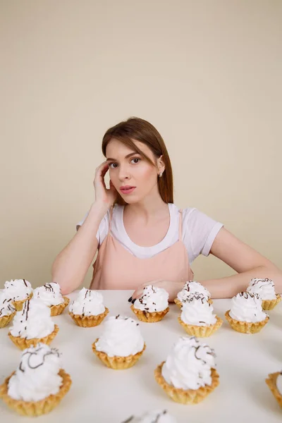 Hübsche junge Frau posiert in der Nähe von Cupcakes auf dem Tisch — Stockfoto