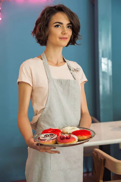 Jovem garçonete bonita em avental servindo donuts em uma bandeja — Fotografia de Stock