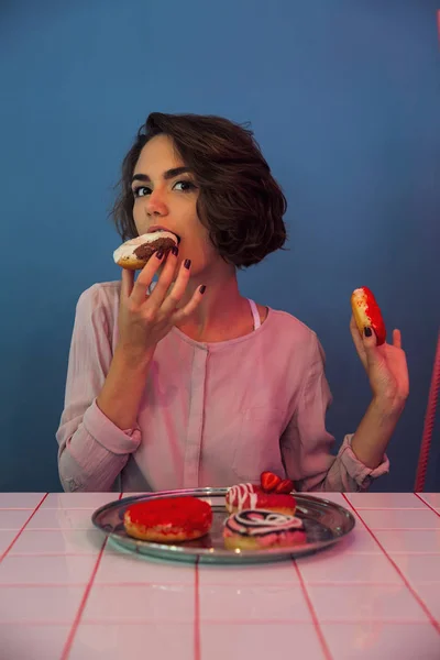 Fată tânără flămândă mănâncă gogoși la masă — Fotografie, imagine de stoc