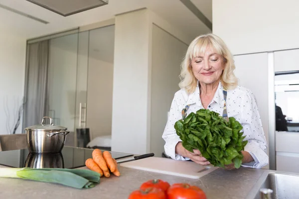 Mujer mayor sonriente preparando ensalada en la cocina — Foto de Stock