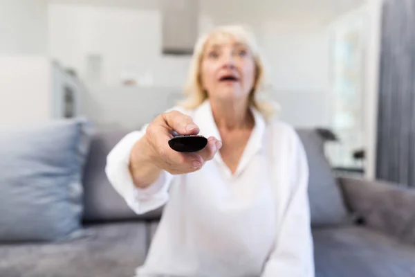 Starší žena mění kanál s dálkovým ovládáním doma — Stock fotografie