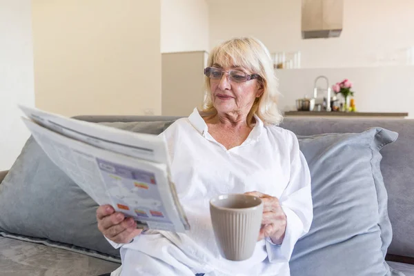 Starší žena v brýlích, čte noviny — Stock fotografie
