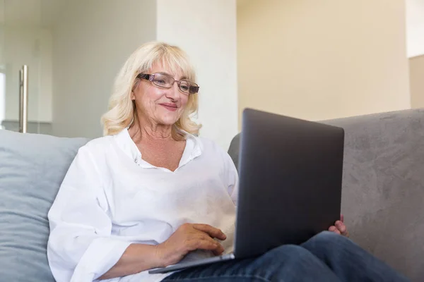 Улыбающаяся пожилая женщина в очках использует ноутбук для работы — стоковое фото