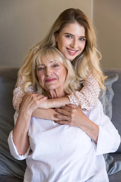 与孙女或女儿拥抱在沙发上的老年妇女 — 图库照片