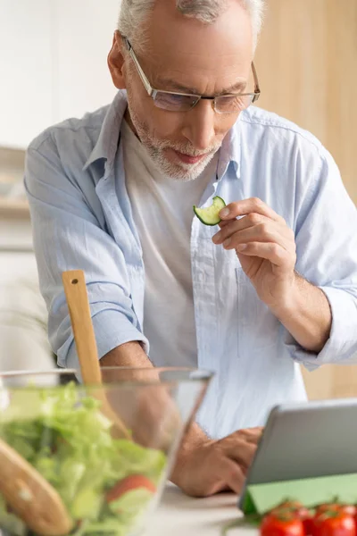 Przystojny skoncentrowane dojrzały mężczyzna gotowanie Sałatka za pomocą tabletu — Zdjęcie stockowe