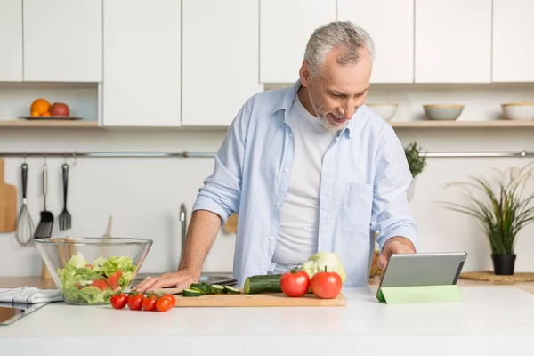 サラダを調理する台所に立っているハンサムな中年の男性. — ストック写真