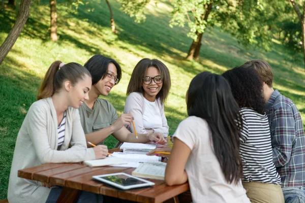 Jovens estudantes sentados e estudando ao ar livre enquanto conversam . — Fotografia de Stock