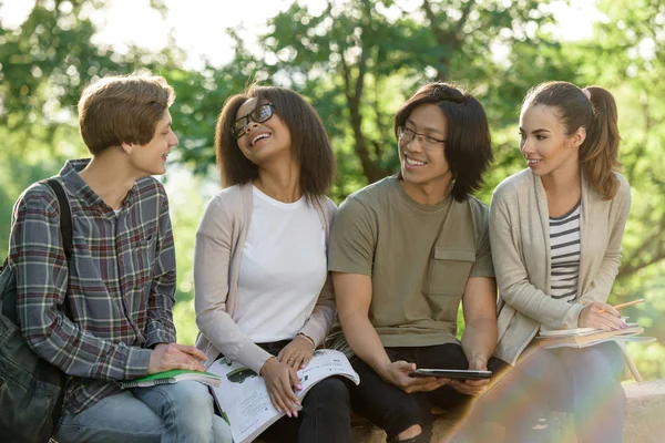 Jonge vrolijke studenten zitten en studeren buiten — Stockfoto