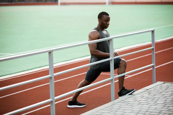 Joven atleta africano concentrado estirando las piernas antes de la competición — Foto de Stock