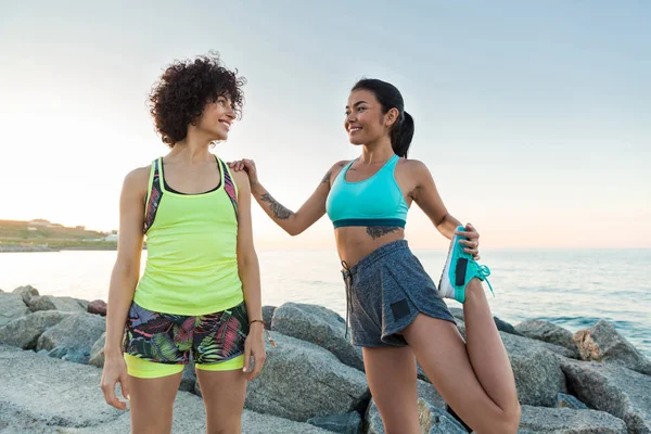 Två unga idrottskvinnor stretching på stranden — Stockfoto