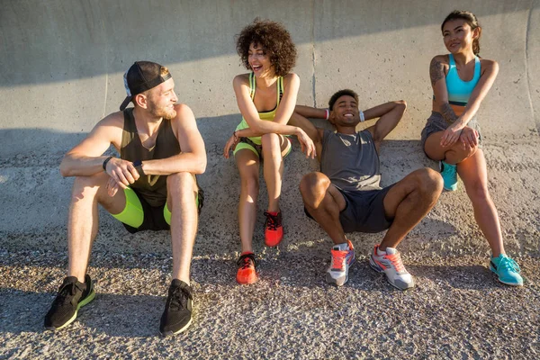 Group of young friends in sportswear resting and talking outdoors — Stock Photo, Image