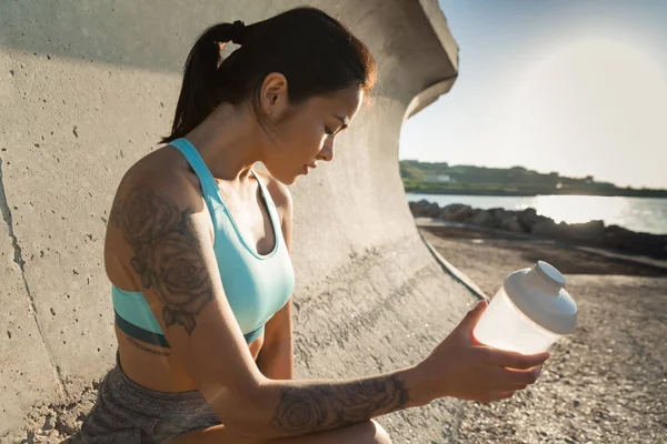 Ung trött fitness kvinna sitter och innehar vattenflaska — Stockfoto