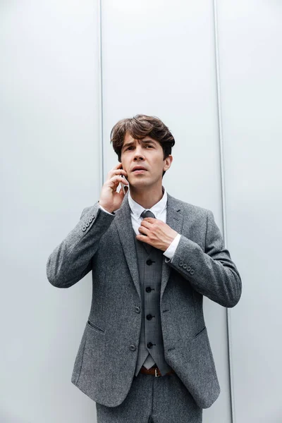 Hombre de negocios guapo en traje de pie y hablando en el teléfono móvil —  Fotos de Stock