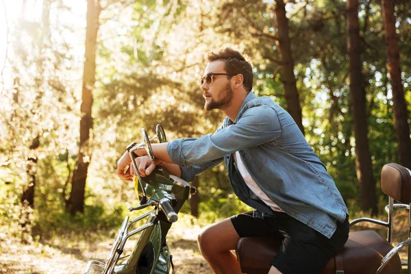 Schöner junger bärtiger Mann sitzt auf Motorroller im Freien — Stockfoto