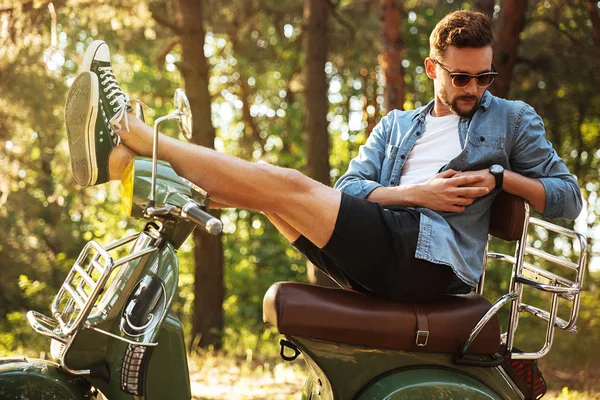 Красивий молодий бородатий чоловік сидить на скутері на відкритому повітрі — стокове фото