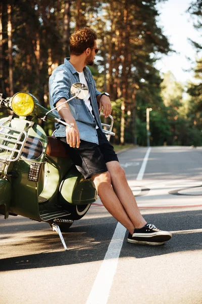 Beau jeune homme barbu debout près de scooter à l'extérieur — Photo