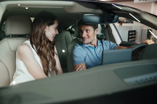 Pareja joven sentada dentro de coche nuevo — Foto de Stock