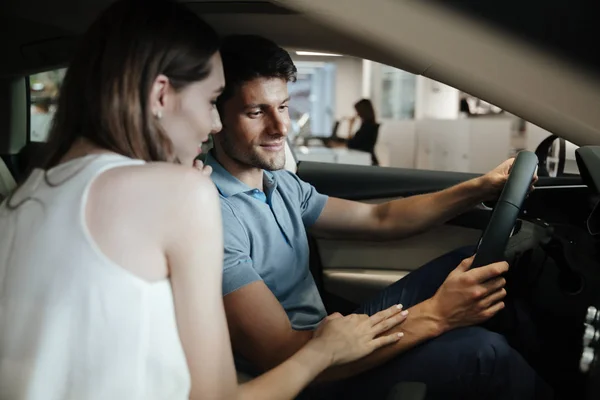 Giovane coppia sorridente seduta ai sedili anteriori della loro nuova auto — Foto Stock