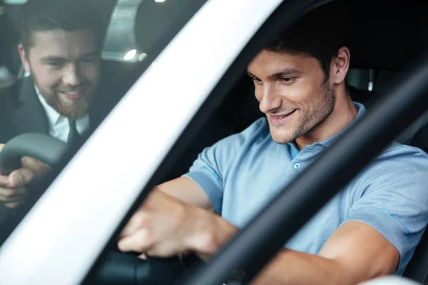 Joven pareja sonriente probando un coche nuevo mientras está sentado dentro —  Fotos de Stock