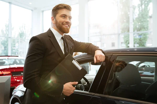 Sonriente vendedor de coches joven de pie en el concesionario —  Fotos de Stock