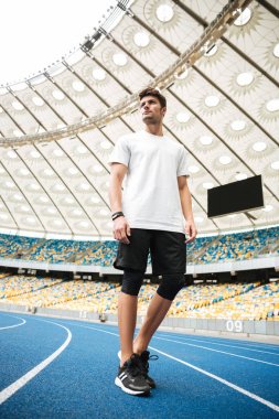 Bir yarış pisti üzerinde yürüyen bir genç sporcu, düşük açılı görünüş