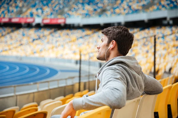 Vista lateral del joven en ropa deportiva con auriculares sentados — Foto de Stock