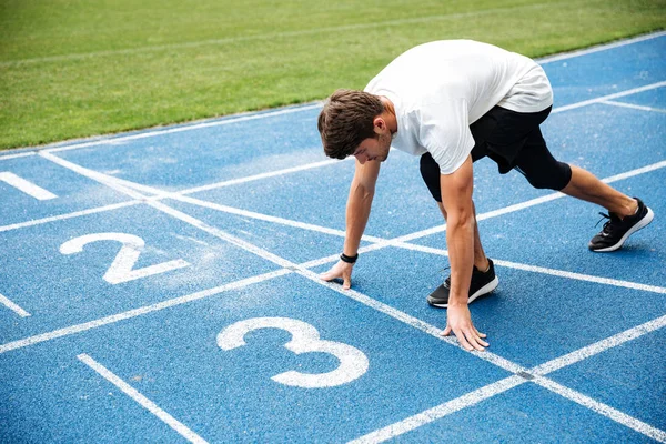 Jovem em pé na posição inicial para correr na pista — Fotografia de Stock