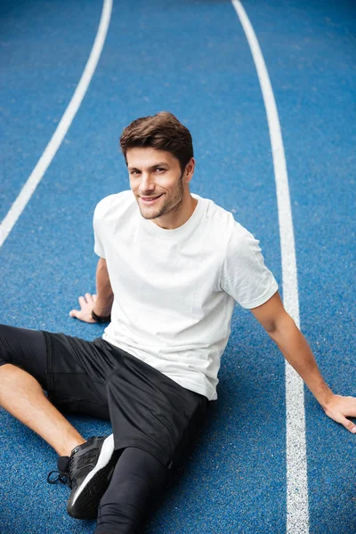 Sorridente giovane sportivo seduto allo stadio — Foto Stock