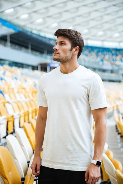 Hombre deportivo de pie en el estadio al aire libre y mirando a un lado . — Foto de Stock
