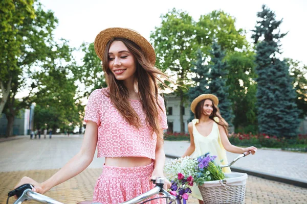 Two young happy ladies standing outdoors with bicycles — Stock Photo, Image