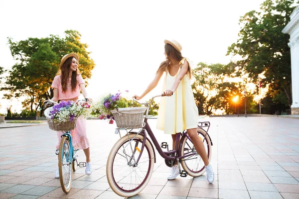 Two young pretty women in dresses sitting on retro bicycles — Stock Photo, Image