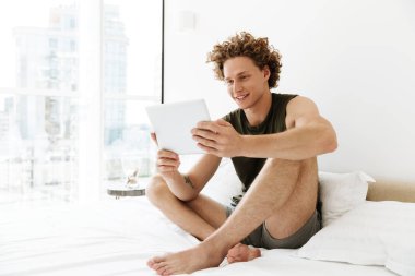 Mutlu adam yatakta evde oturan tablet bilgisayar kullanarak