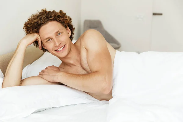 Schöner junger Mann liegt im Bett und schaut in die Kamera — Stockfoto