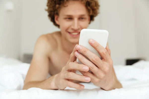 Alegre guapo hombre se encuentra en la cama charlando por teléfono — Foto de Stock