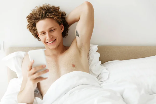 Красивый улыбающийся мужчина отправляет сообщение на мобильный телефон — стоковое фото