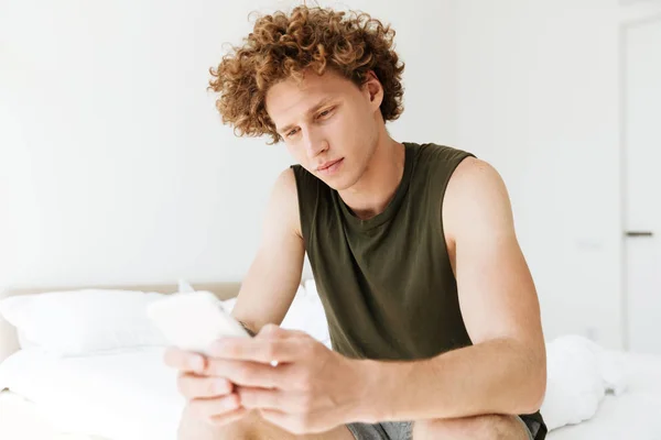 Yakışıklı adam yatakta evde oturan telefonla sohbet — Stok fotoğraf