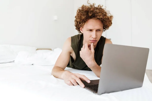 Konsantre adam evde yatakta yatıyor dizüstü bilgisayar kullanarak — Stok fotoğraf