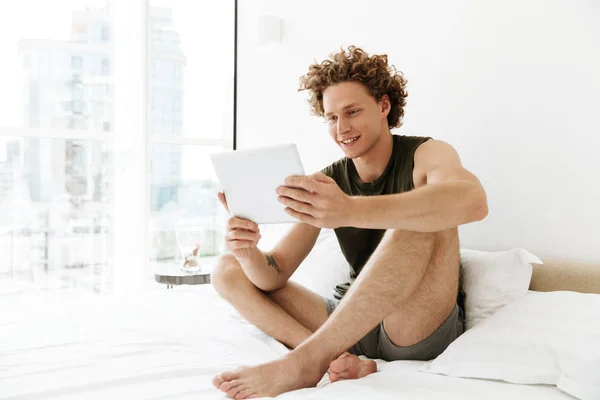 Hombre feliz sentado en la cama en casa usando tableta — Foto de Stock