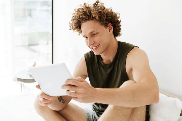 Счастливый мужчина сидит дома на кровати с помощью планшетного компьютера — стоковое фото