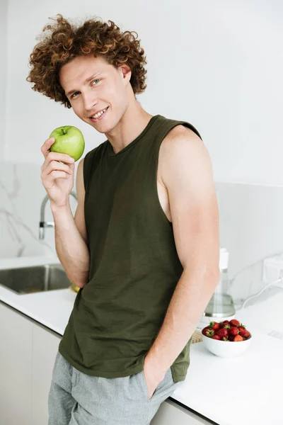 Sorrindo homem de pé na cozinha e segurando maçã — Fotografia de Stock