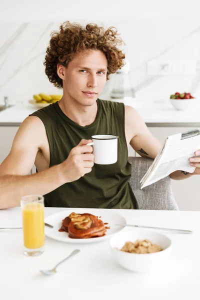 Homme assis à la cuisine tout en tenant le journal — Photo