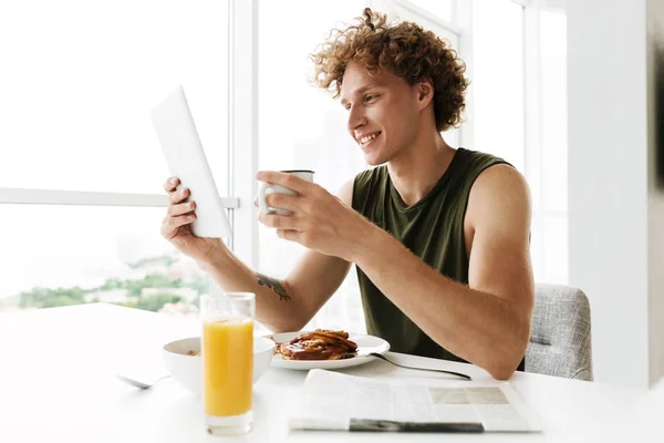 Bonito homem feliz usando computador tablet e beber café — Fotografia de Stock