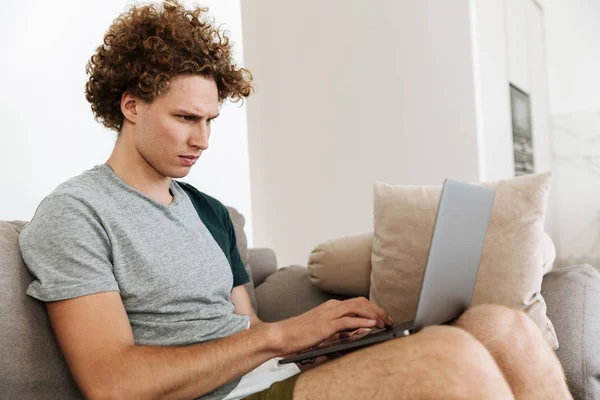 Knappe geconcentreerde man zit op de Bank met behulp van laptop — Stockfoto