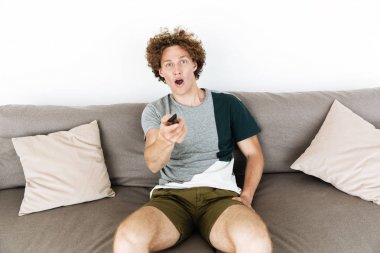 Uzaktan kumanda tutan koltukta oturan yakışıklı şok adam