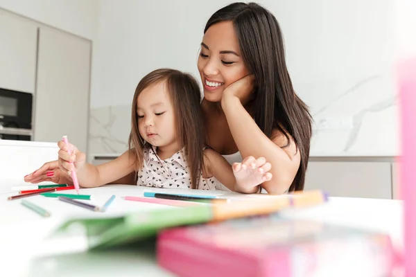 Lächelnde Asiatin, die ihrer kleinen Tochter das Zeichnen beibringt — Stockfoto